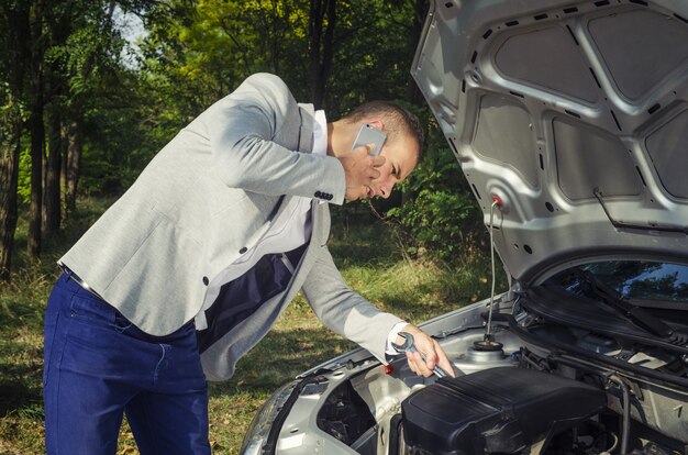 Man standing by the open hood making a phone call and trying to fix the vehicle