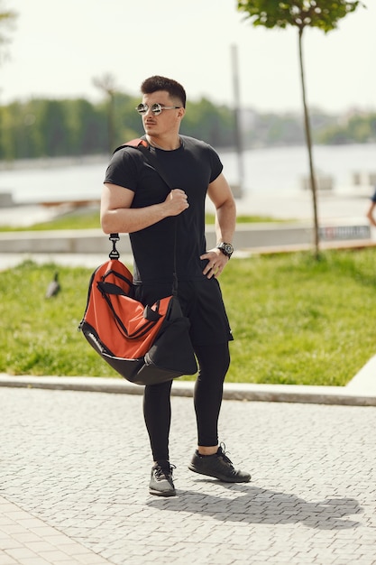 Man standing by the water. Guy in a sports clothes. Male in a summer park with backpack