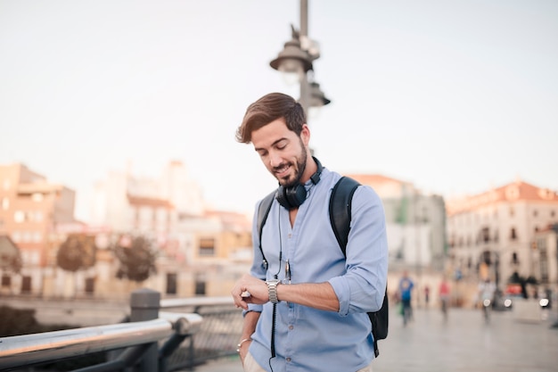 Free photo man standing in front of city building looking at time on watch