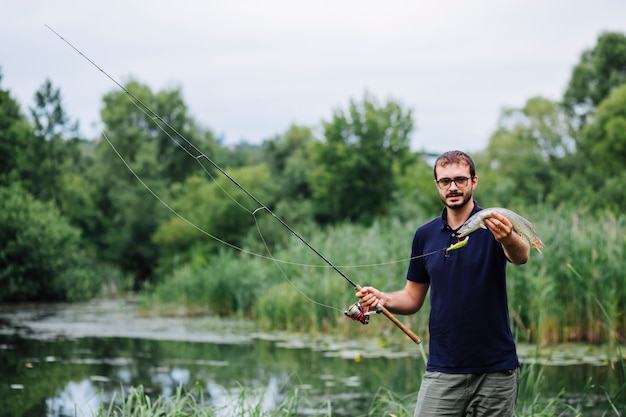 Free photo man standing in front of lake holding caught fresh fish