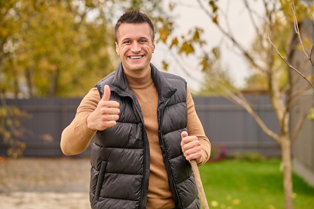 Free photo man standing in garden showing ok gesture looking at camera