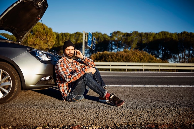 壊れた車の隣に立っている男性