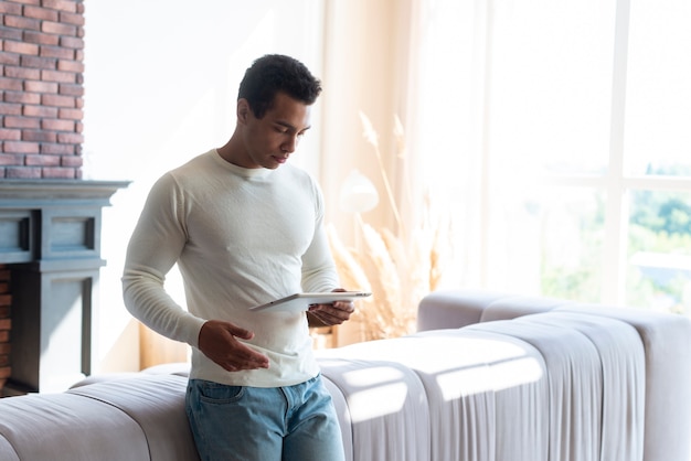 Man standing in living and holding tablet