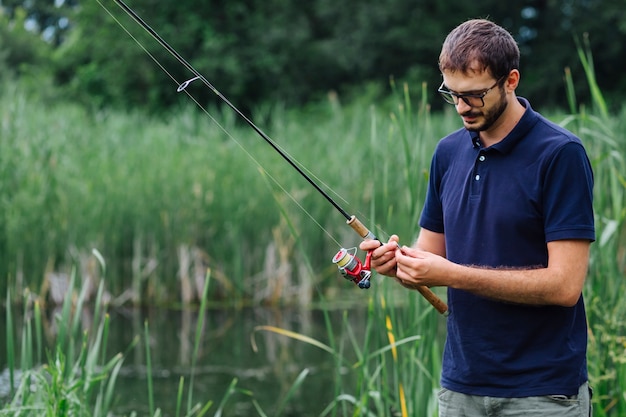 Man standing near lake tying fishing bait on rod