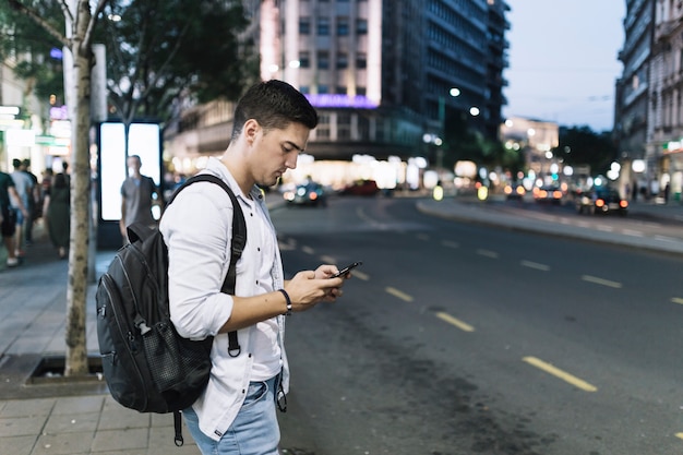 Foto gratuita equipaggi la condizione sul bordo della strada che esamina lo schermo del telefono cellulare