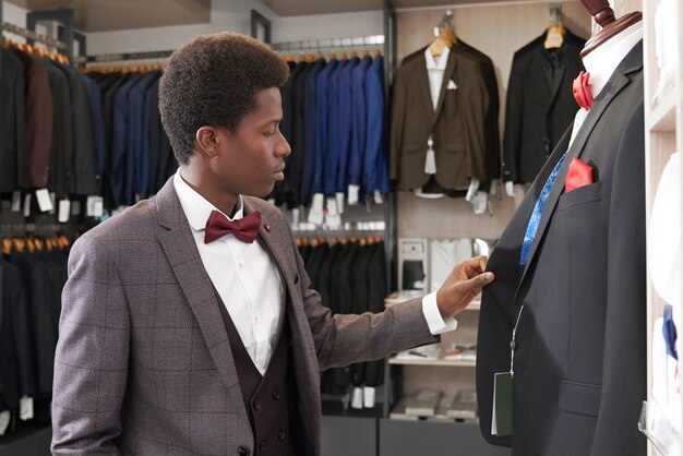 Man standing in shop with clothing near mannequin.