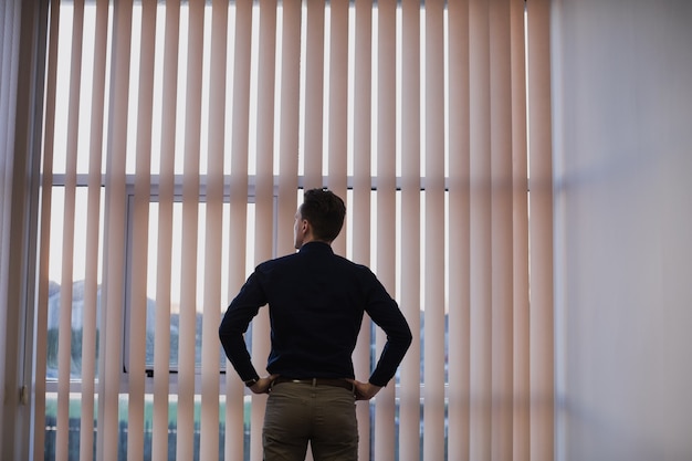 Man standing with hands on hip near window blinds