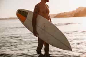 Foto gratuita uomo in piedi con tavola da surf in mare