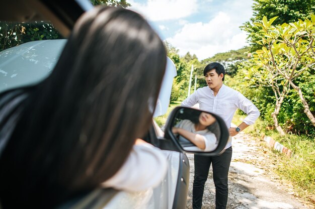 男は壊れた車を見て立っており、女性はその中に座っています。