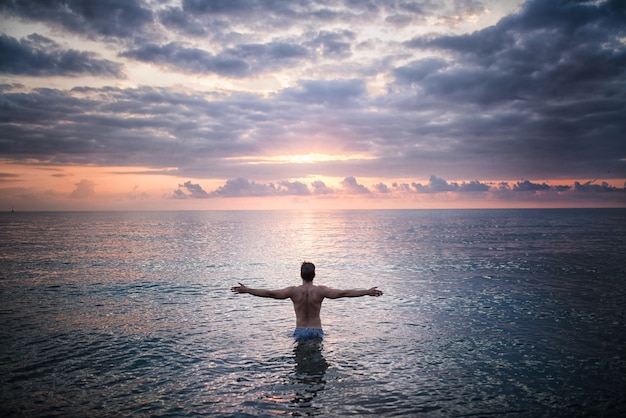 Man stands in the sea water facing sunset