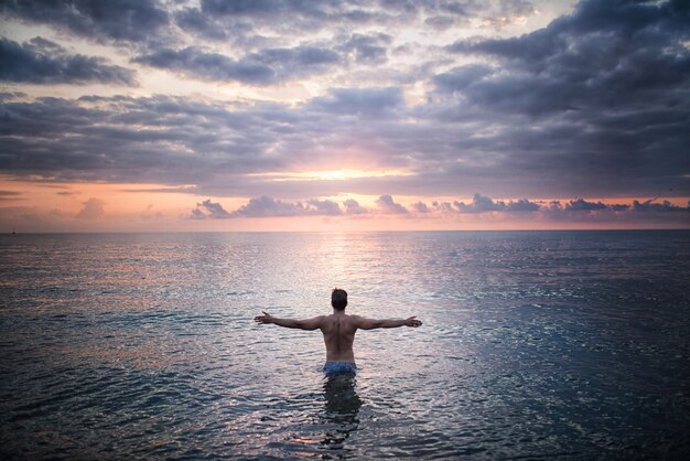 人は夕日に面した海水に立っている