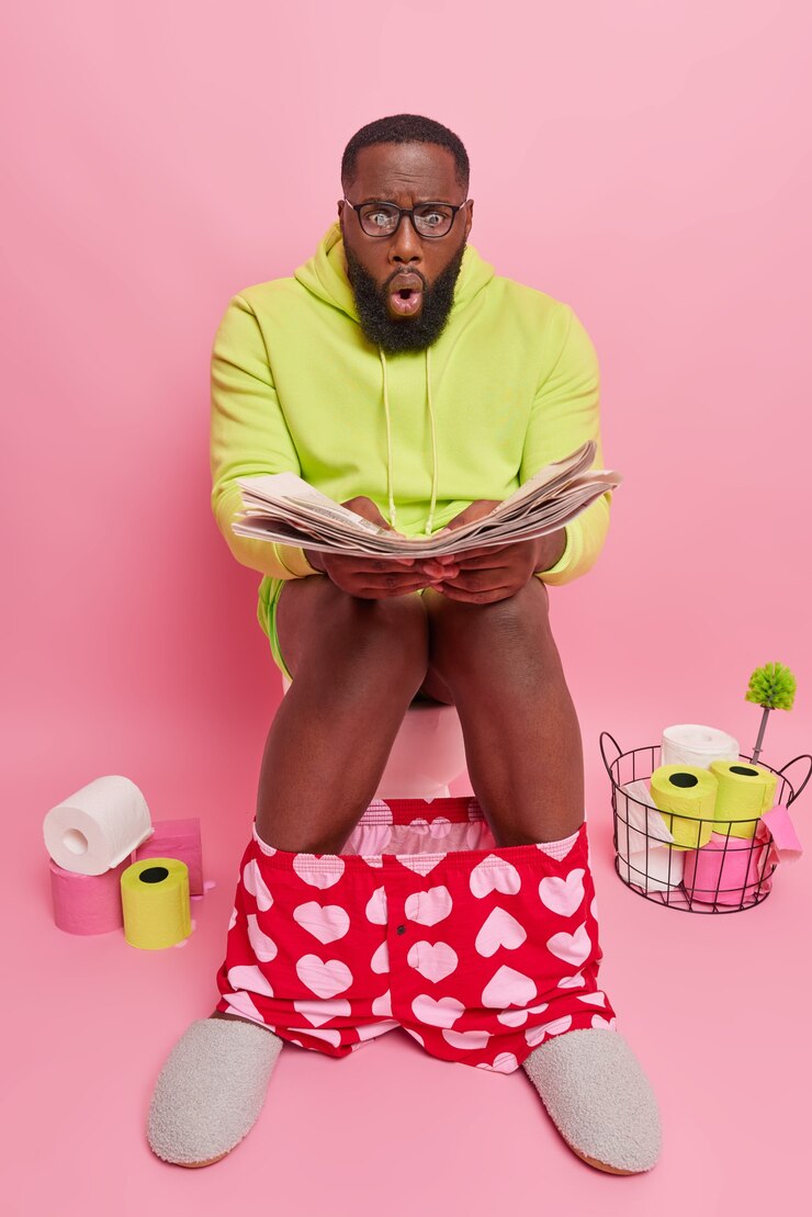 Free Photo  man stares at newspaper reads article with embarrassing news wears big transparent glasses for vision correction dressed in domestic clothes sits on toilet bowl in restroom