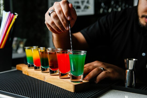 Man stirs the colorful shots green red yellow orange