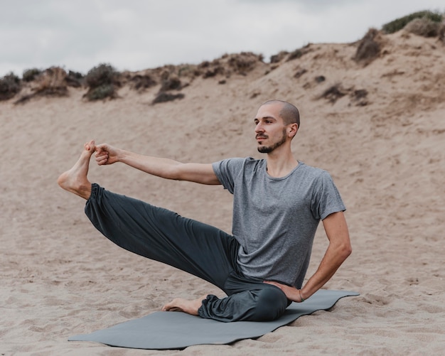 Free photo man stretching his leg while doing yoga outdoors