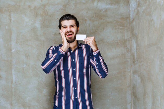 Man in striped shirt holding his business card and feels surprised