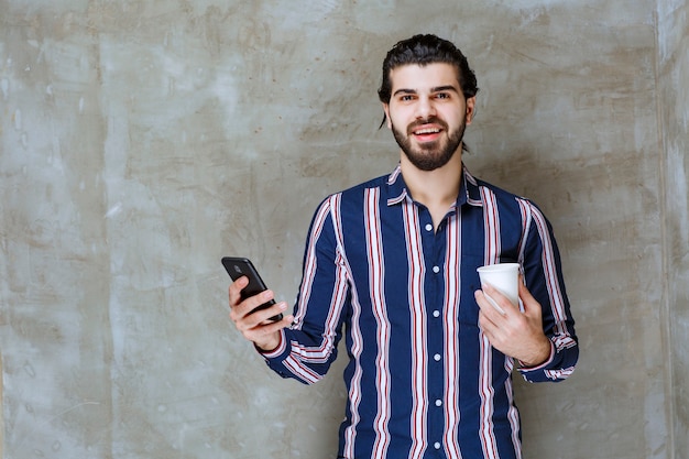 Man in striped shirt holding a water cup and playing with his phone