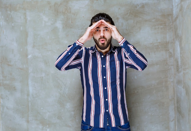 Foto gratuita uomo in camicia a righe che mette mano alla fronte e osserva.