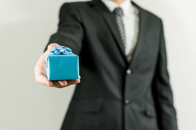 man in a suit holding a blue small present box