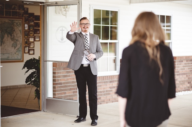 Man in suit outside a church waving and welcoming a woman