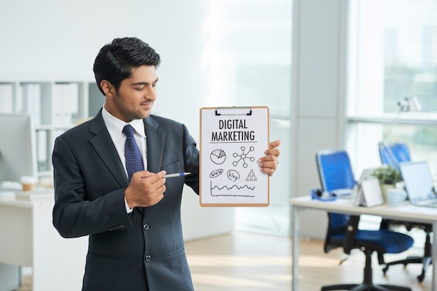 Free photo man in suit standing in office with clipboard and pointing to poster with words