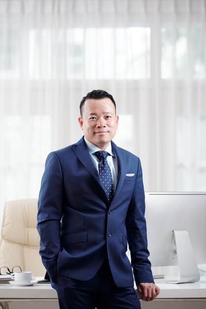 Man in suit and tie standing at his office table showing off his success