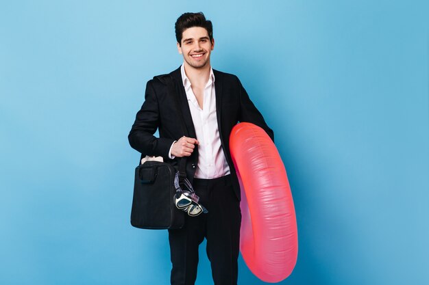 Man in suit with laptop bag holds diving mask and rubber ring. Guy wants to rest.