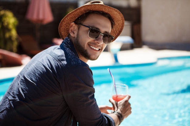 サングラスと帽子を飲んでカクテル、プールのそばに座っている男