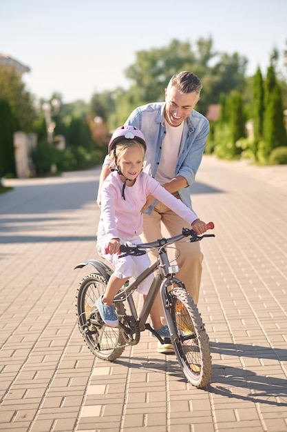 A man supporting a girl while she riding a bike