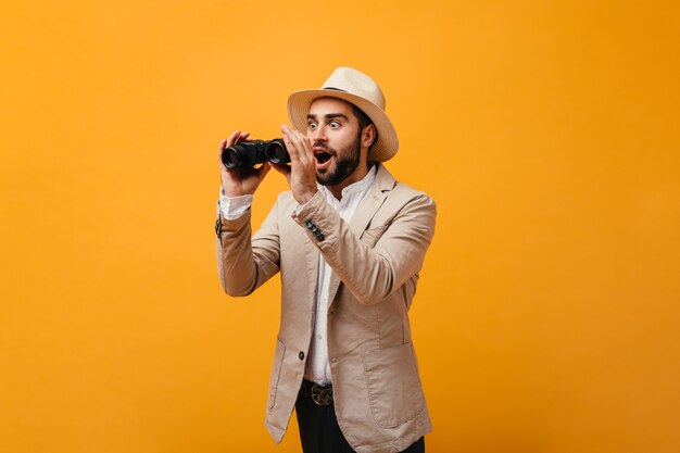 Man surprised looks into binoculars on isolated wall