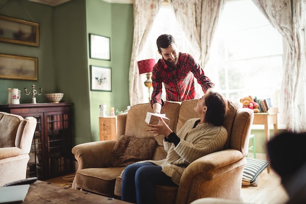 Man surprising woman with a gift in living room