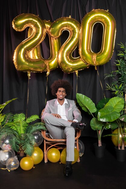 Man surrounded by happy new year 2020 golden balloons