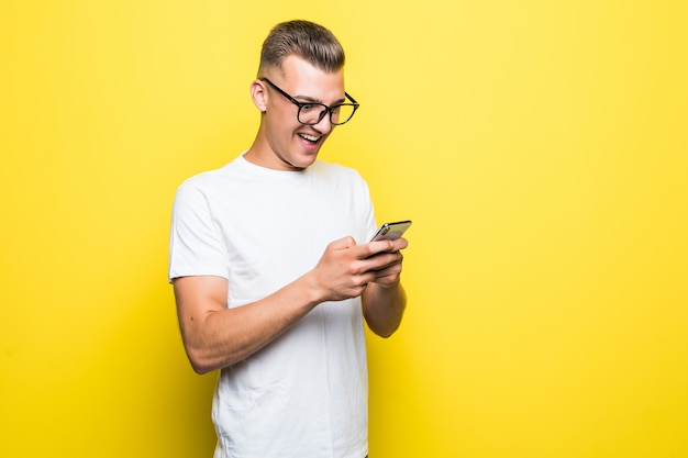 Man in t-shirt and glasses makes something on his phone and takes selfie pictures isolated on yellow background