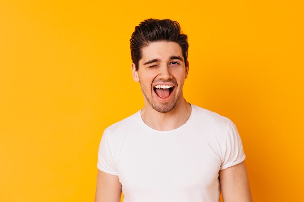 Мужчина в футболке в хорошем настроении подмигивает на фоне оранжевого пространства.