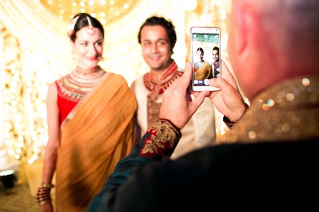 Человек фотографирует индусскую свадебную пару на своем смартфоне