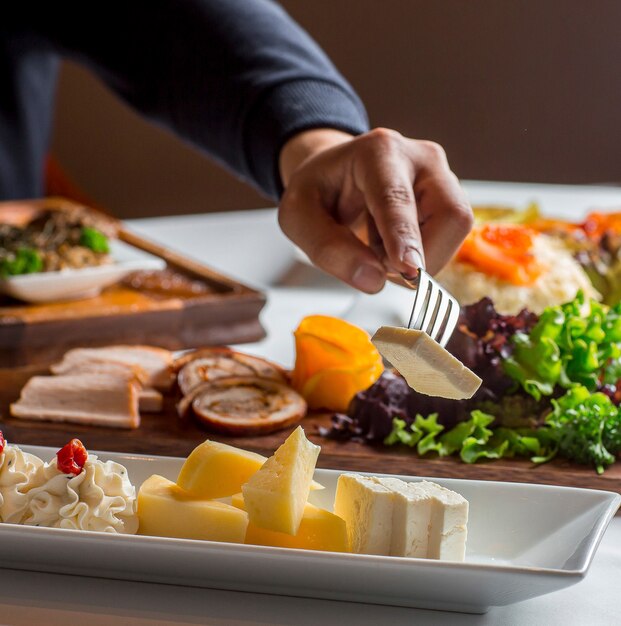 Man taking cheese from cheese plate with white cheese, cheddar, cream cheese