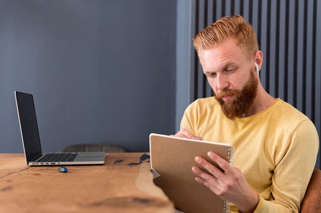 Free photo man taking notes while using earbuds