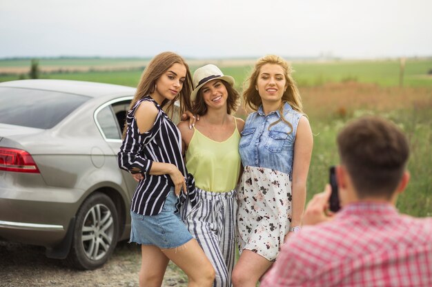 Человек с фотографией трех женщин-друзей, стоящих рядом с автомобилем