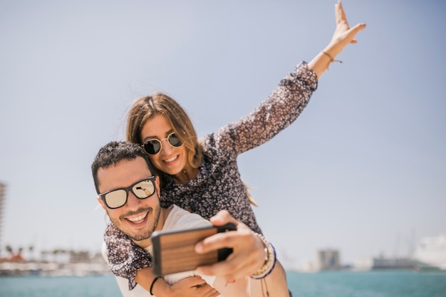 Man taking photograph of her girlfriend enjoying piggyback ride on his back