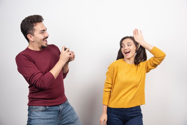 Man taking a picture of young woman on a white wall.