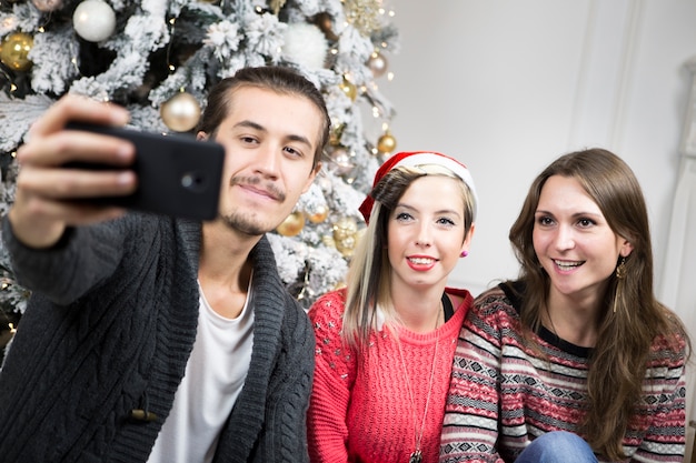 Man taking selfie of friends in front of christmas tree
