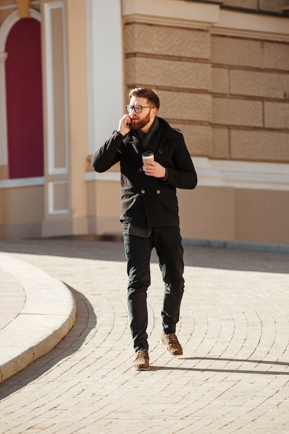 Man talking on mobile phone and drinking coffee in city