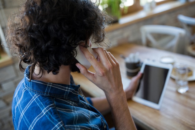 Man talking on the mobile phone and looking at digital tablet in coffee shop