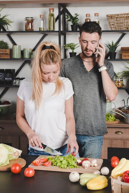 キッチンにナイフで野菜を切る妻を見て携帯電話で話す男