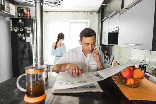 背景に立っている彼の妻と新聞を読んでいる携帯電話で話す男
