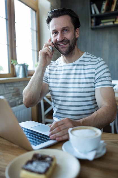 L'uomo parla al telefono cellulare e con laptop in caffetteria