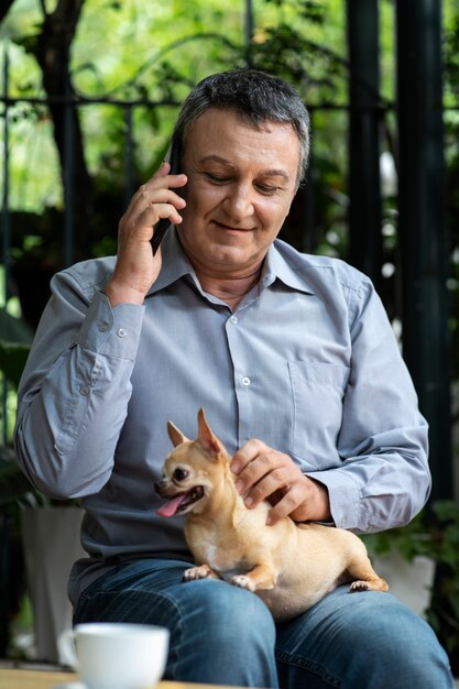 Мужчина разговаривает по телефону в саду, гладя свою собаку
