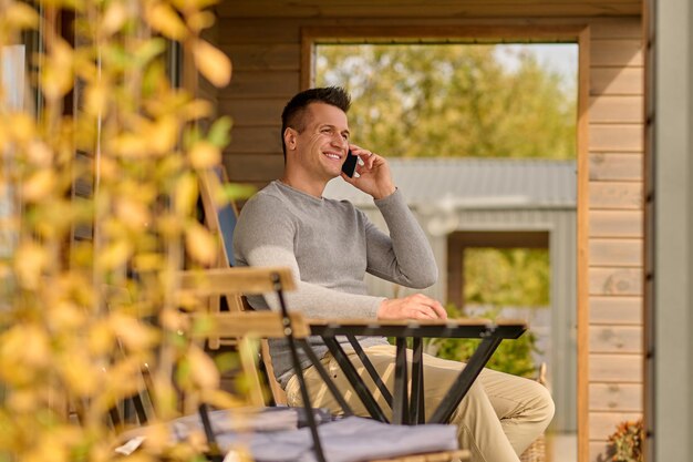 Мужчина разговаривает по смартфону, сидя на открытой террасе