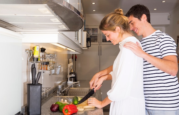 Man teaching her wife to cut vegetables with knife