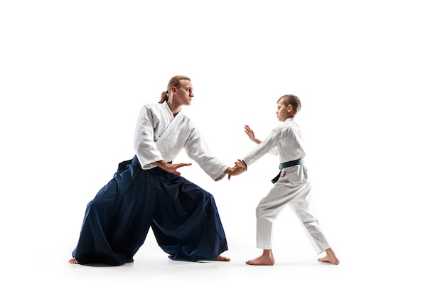 Man and teen boy fighting at Aikido training in martial arts school. Healthy lifestyle and sports concept. Fighters in white kimono on white wall. Karate men with concentrated faces in uniform.