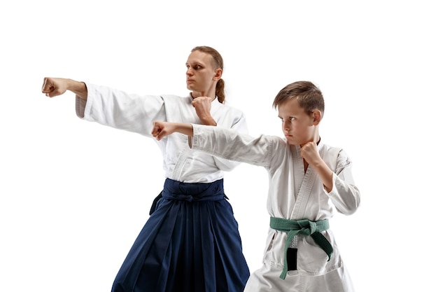 Man and teen boy fighting at Aikido training in martial arts school. Healthy lifestyle and sports concept. Fighters in white kimono on white wall. Karate men with concentrated faces in uniform.